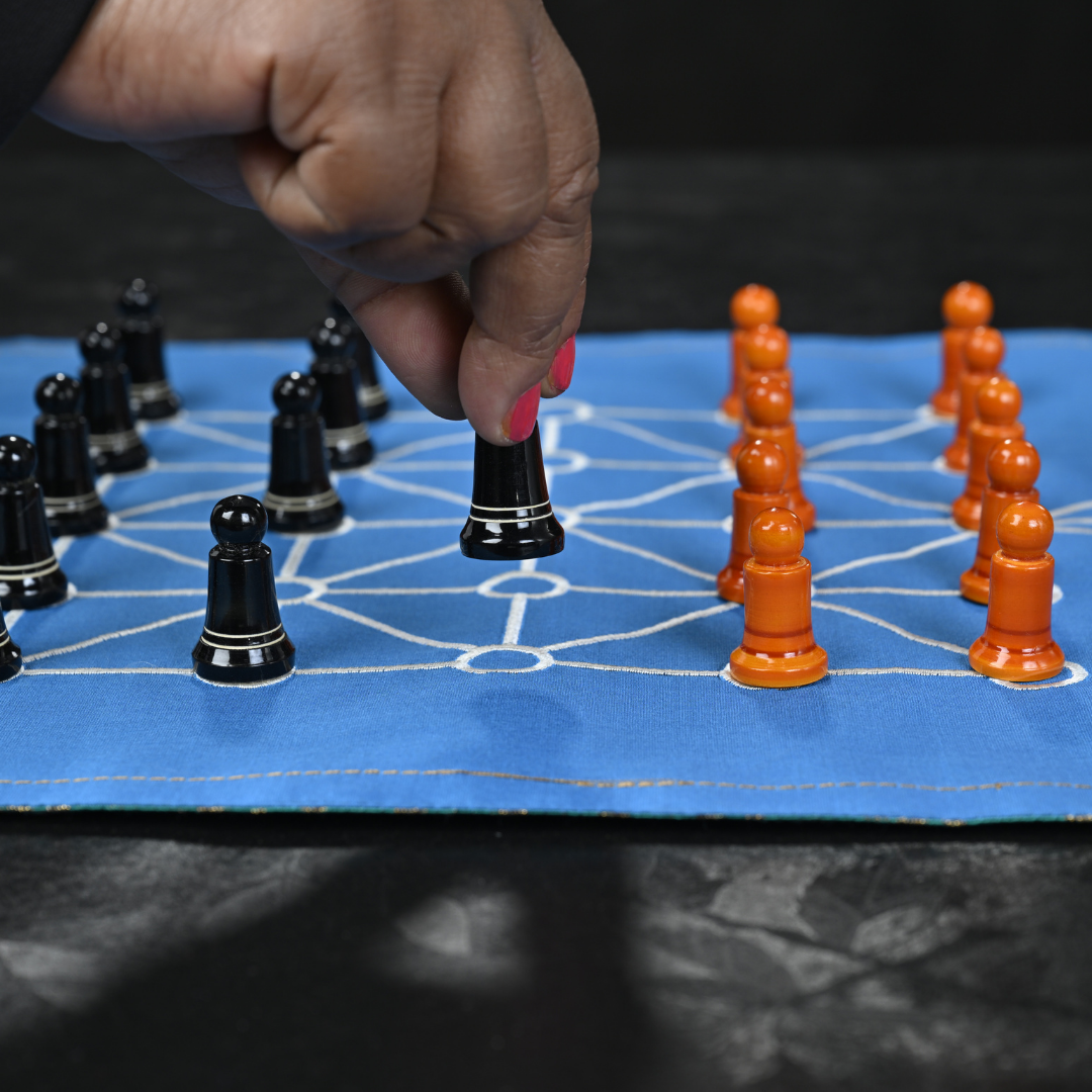 SholoGutti board game featuring sixteen soldiers with colorful game pieces on a wooden board.